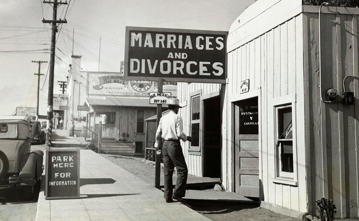 A vintage, black-and-white photo of a man walking into a building with a large "MARRIAGES AND DIVORCES" sign. He's wearing a 