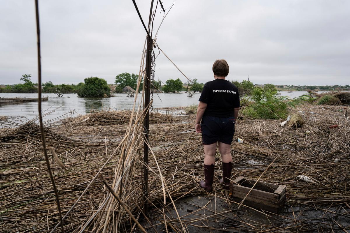 "A resident of Fedorivka is seen standing outside her flooded garden," caused by the collapse of the Kakhovka Dam. She is wea