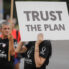 Woman in QAnon shirt holding sign "Trust the plan"