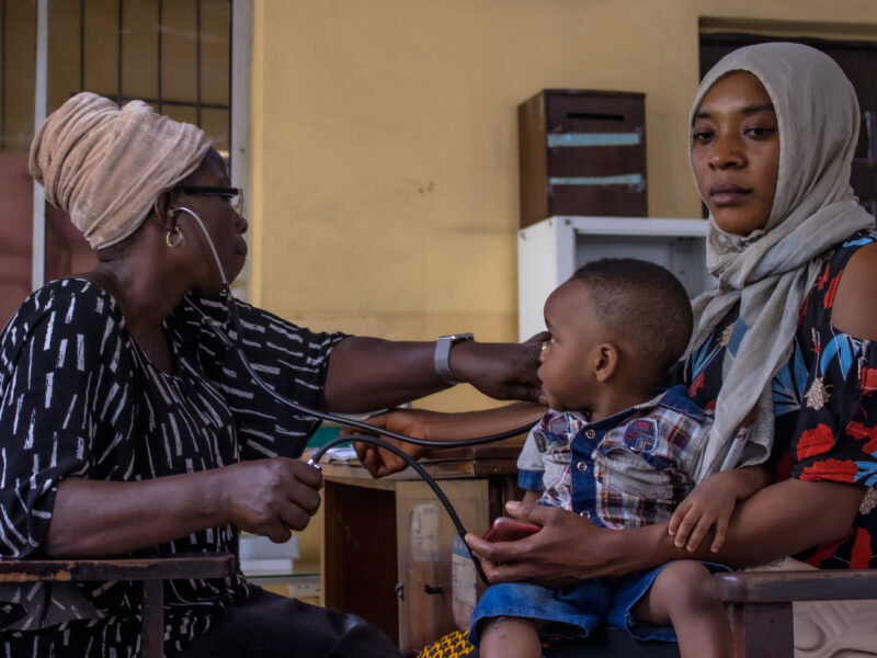 A woman gets her blood pressure checked by an employee at the Planned Parenthood clinic in Isolo, Lagos. A child sits in her lap, curiously watching what is happening.