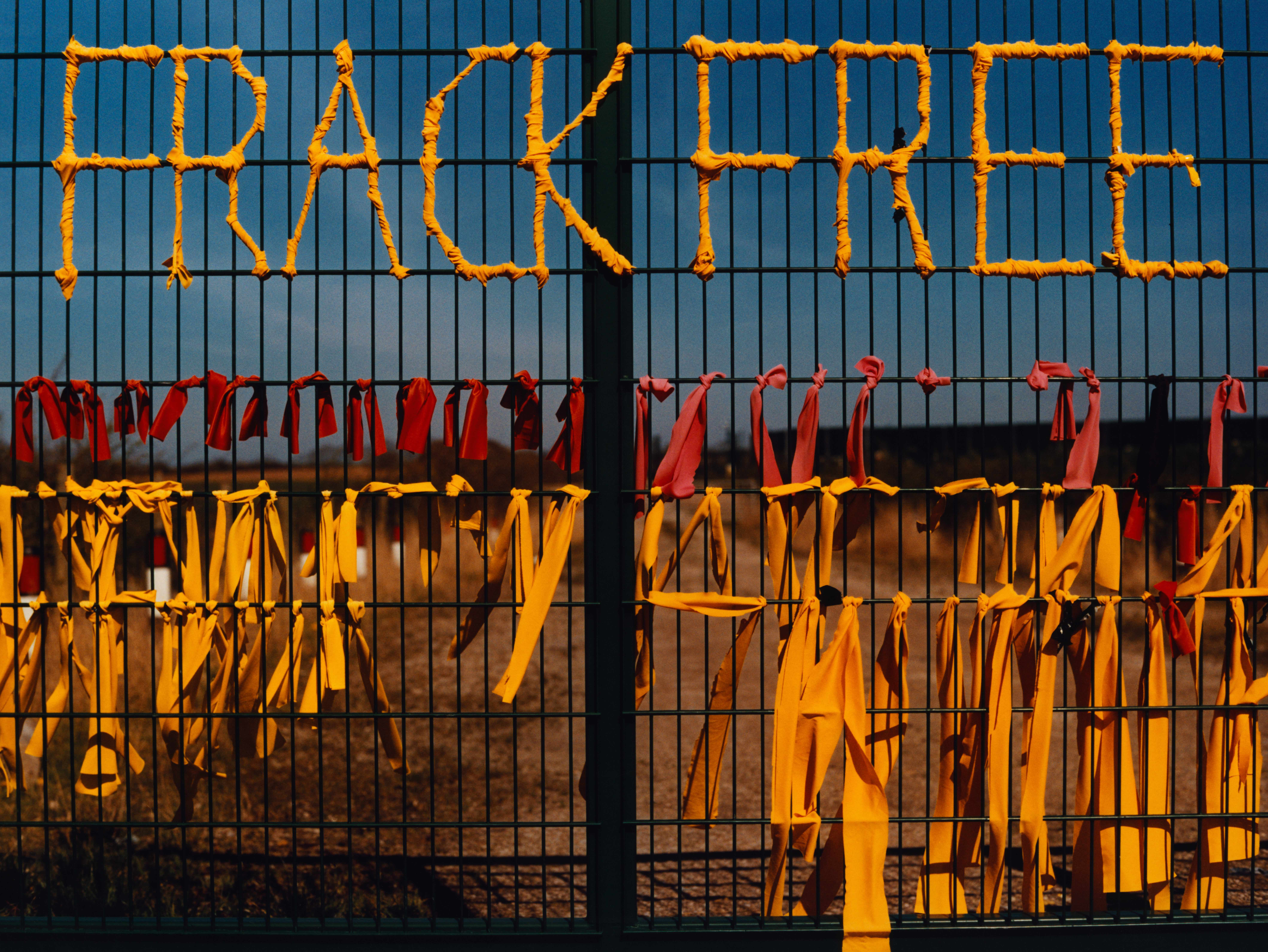 A gate for one of the former fracking sites in the UK. The Nanas have tied dozens of yellow ribbons on the fence, and separately wrapped yellow ribbon so that it spells FRACK FREE. 