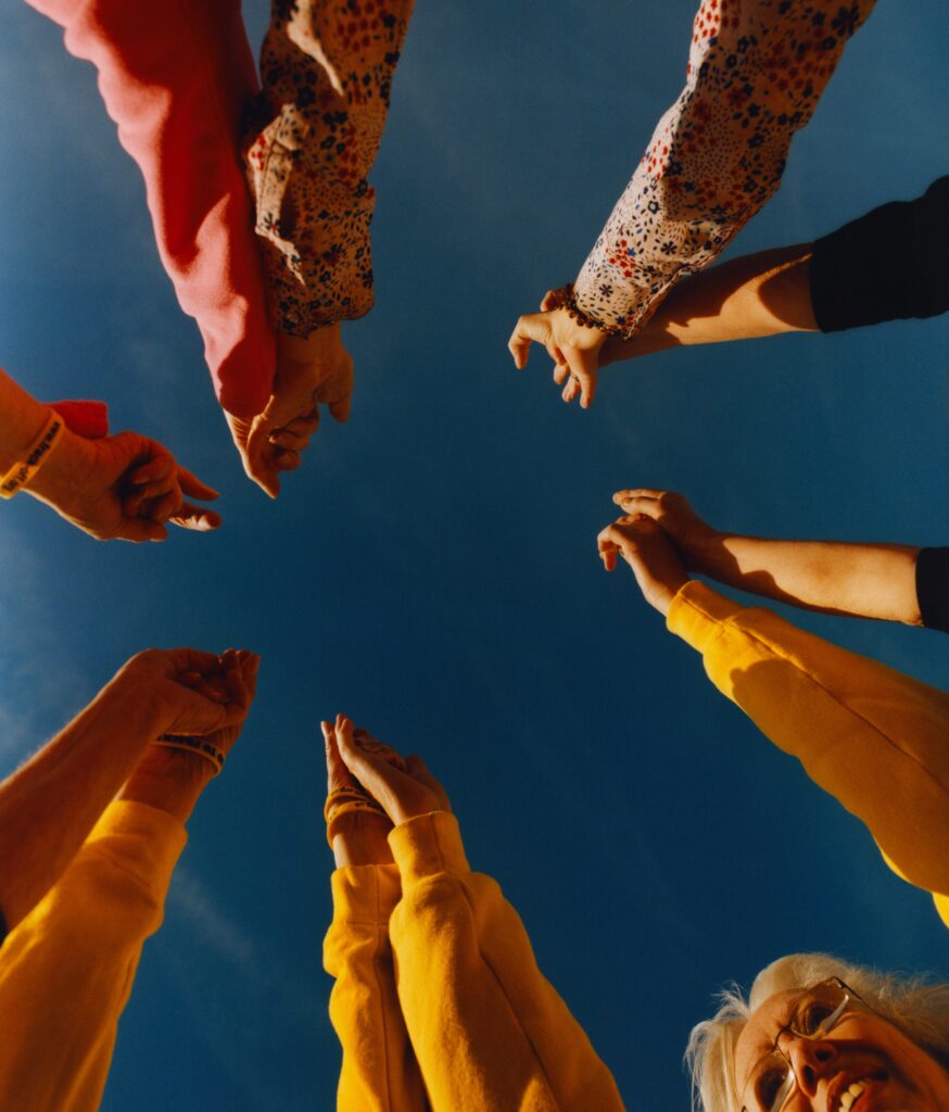 A photograph pointing at a blue sky, from the center of a circle of UK Nanas, holding their hands to the sky.