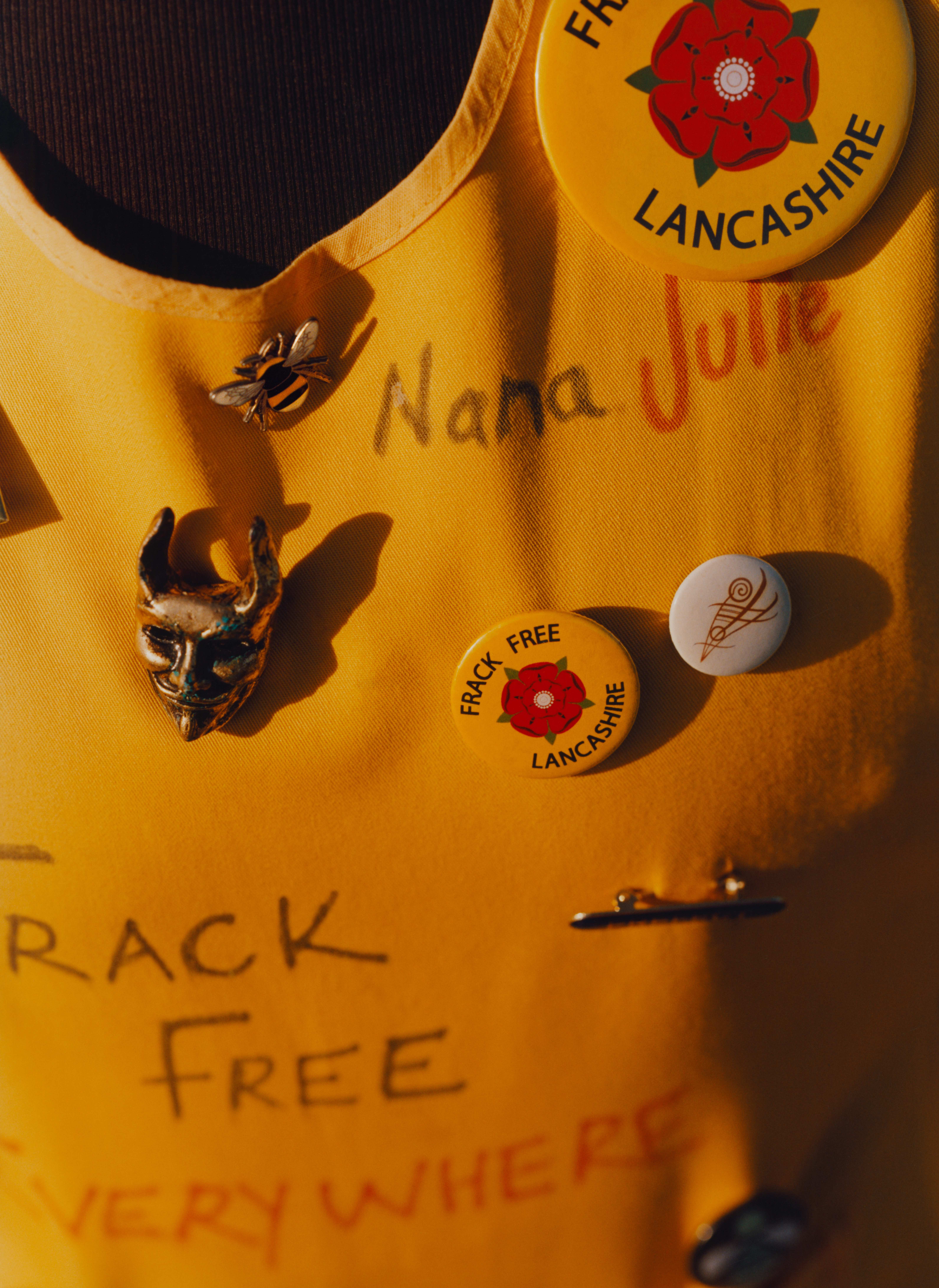 A close-up of one of the UK Nanas' yellow tabards, for "Nana Julie." It has various pins for Frack Free Lancashire, and "FRACK FREE EVERYWHERE" written in Sharpie. 