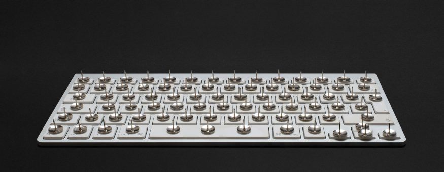 A modern white keyboard on a black background. On each key, there's a thumbtack with the sharp end pointing upwards.
