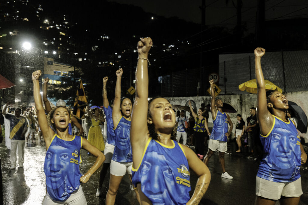 During a street rehearsal by the Unidos da Tijuca samba school, and under heavy rain, the opening performance group performs one of its choreographies from the storyline honoring writer Carolina Maria de Jesus near Favela do Borel, in the Tijuca neighborhood of Rio de Janeiro, Brazil.
