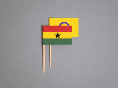 A photo illustration by Ricardo Tomás of Ghana's flag on a toothpick. It is covering the intersex flag (also on a toothpick), starting to rise behind it.