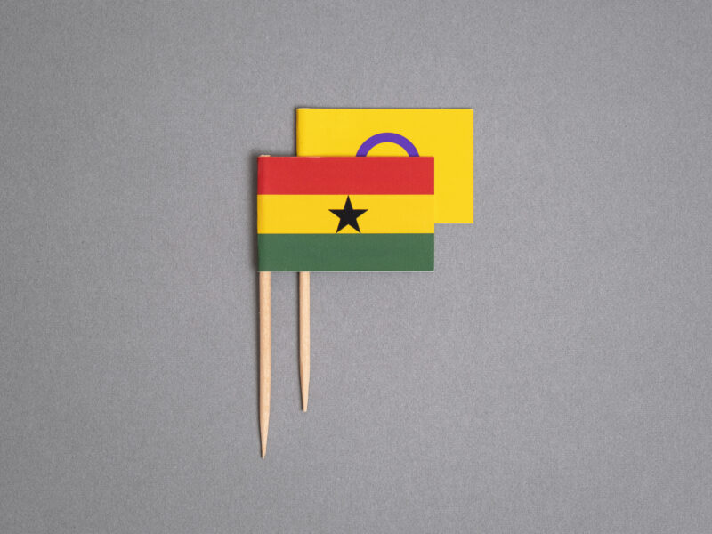 A photo illustration by Ricardo Tomás of Ghana's flag on a toothpick. It is covering the intersex flag (also on a toothpick), starting to rise behind it.