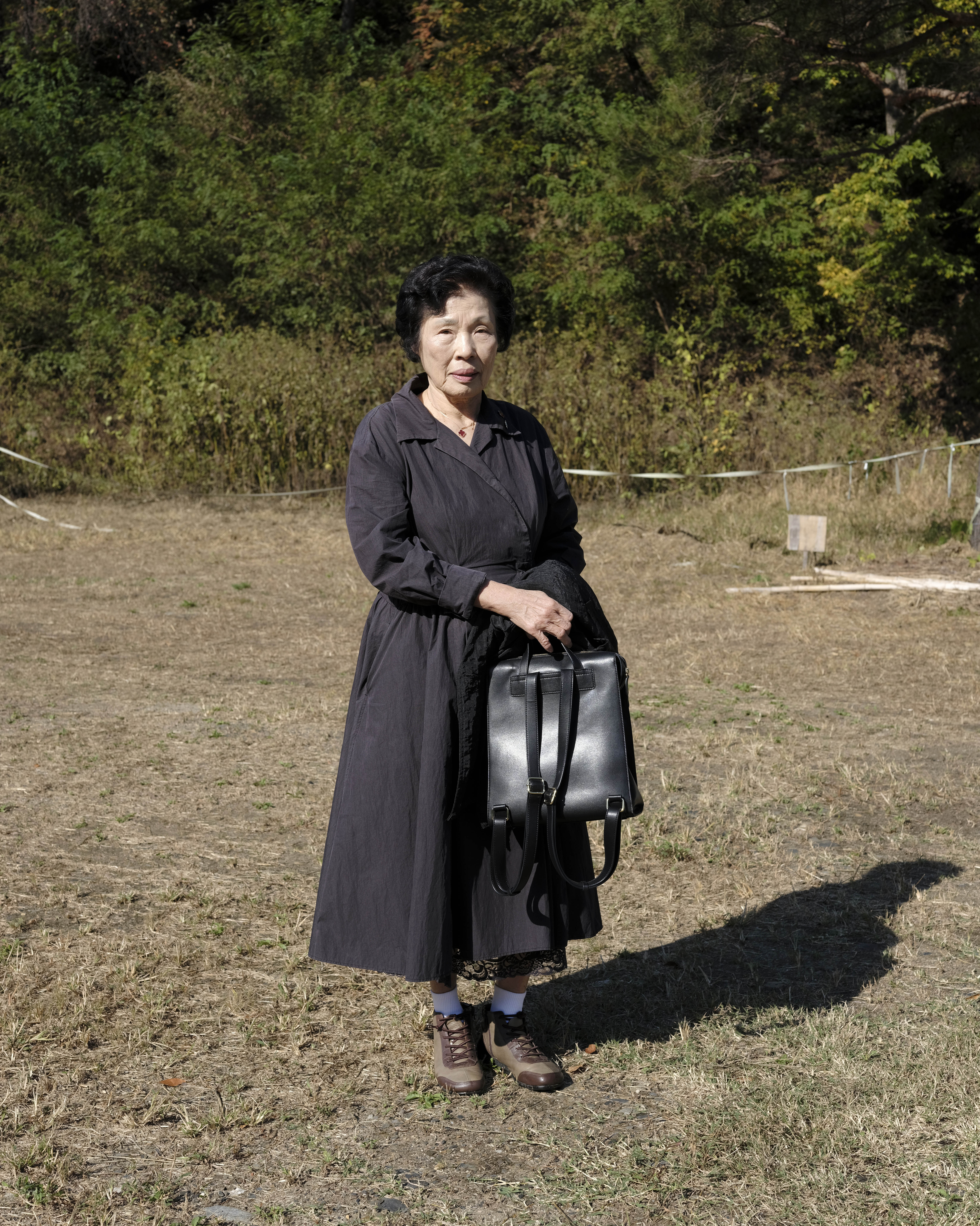 A portrait of Chun Mi Kyung (Chun Imo) standing outside in all black.