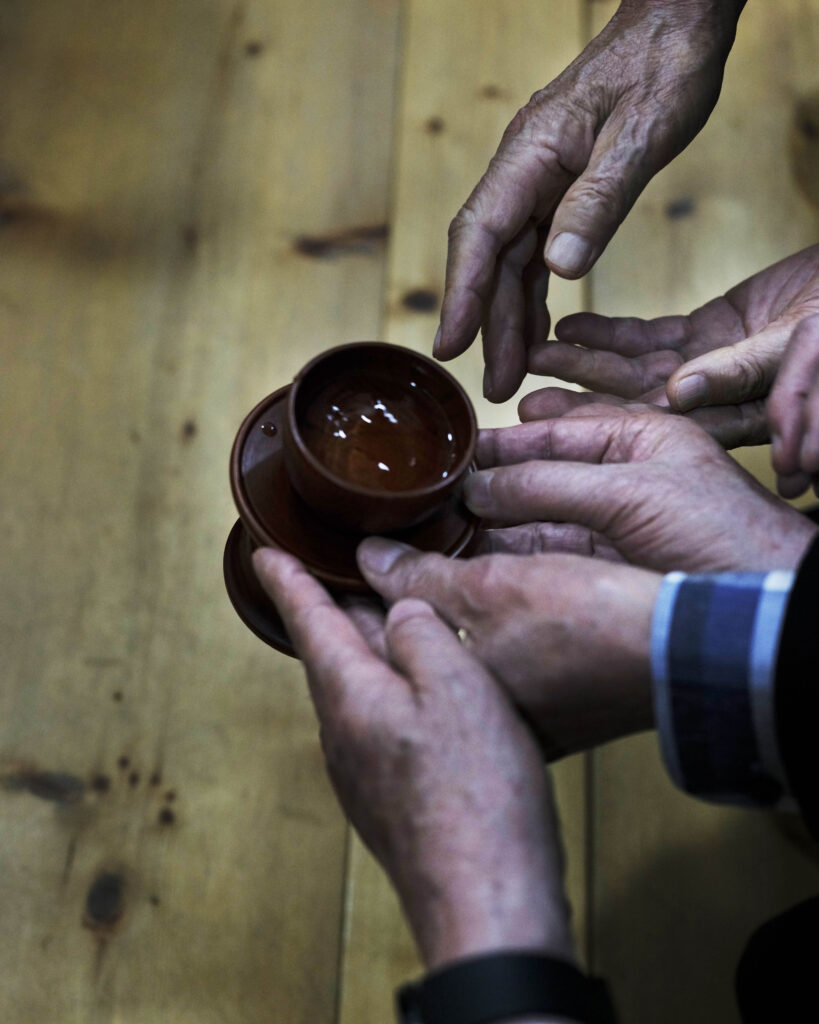 A photo of hands holding a vessels filled it with makkgeolli, 