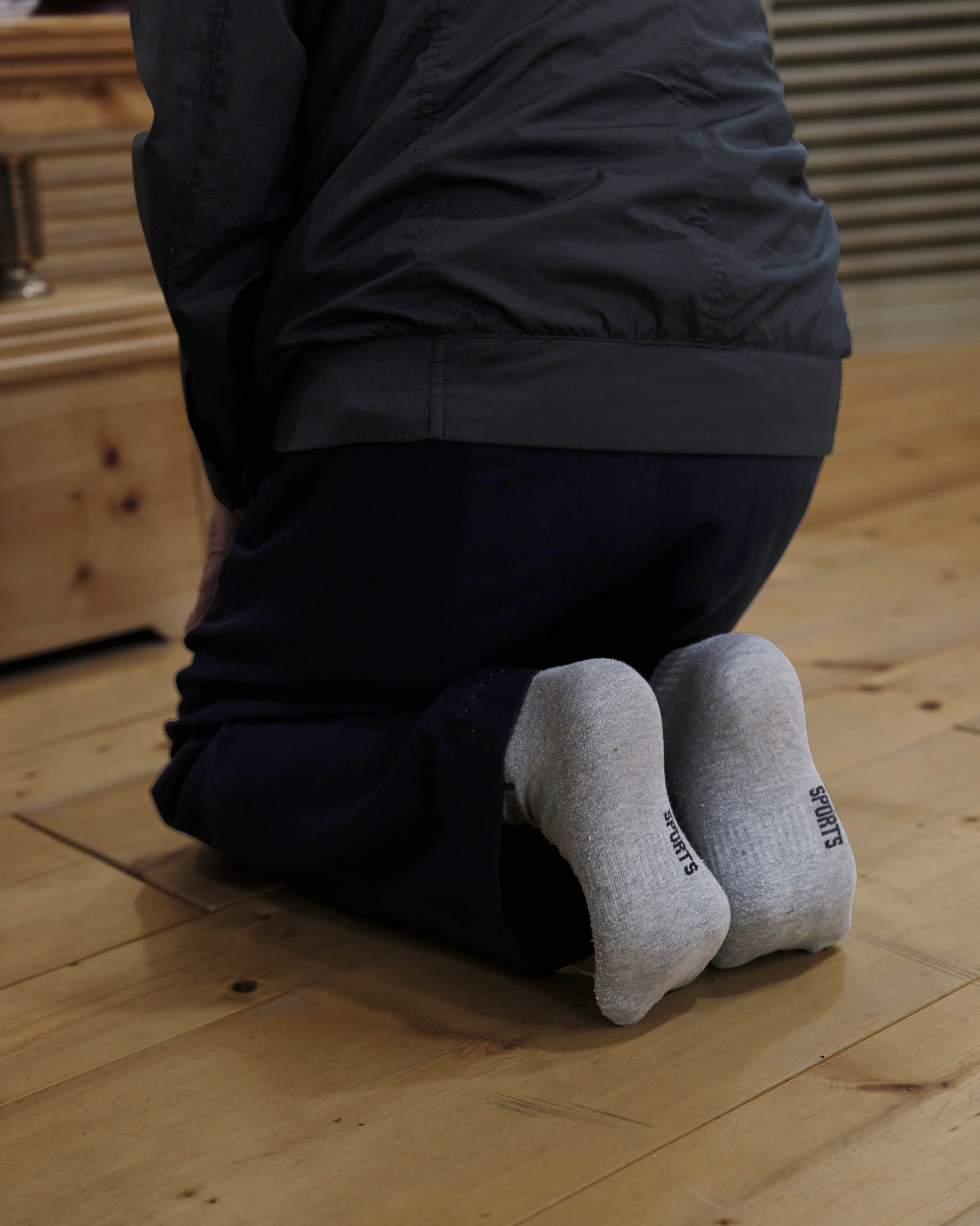 A close-up photo from behind of someone kneeling on a wood floor.