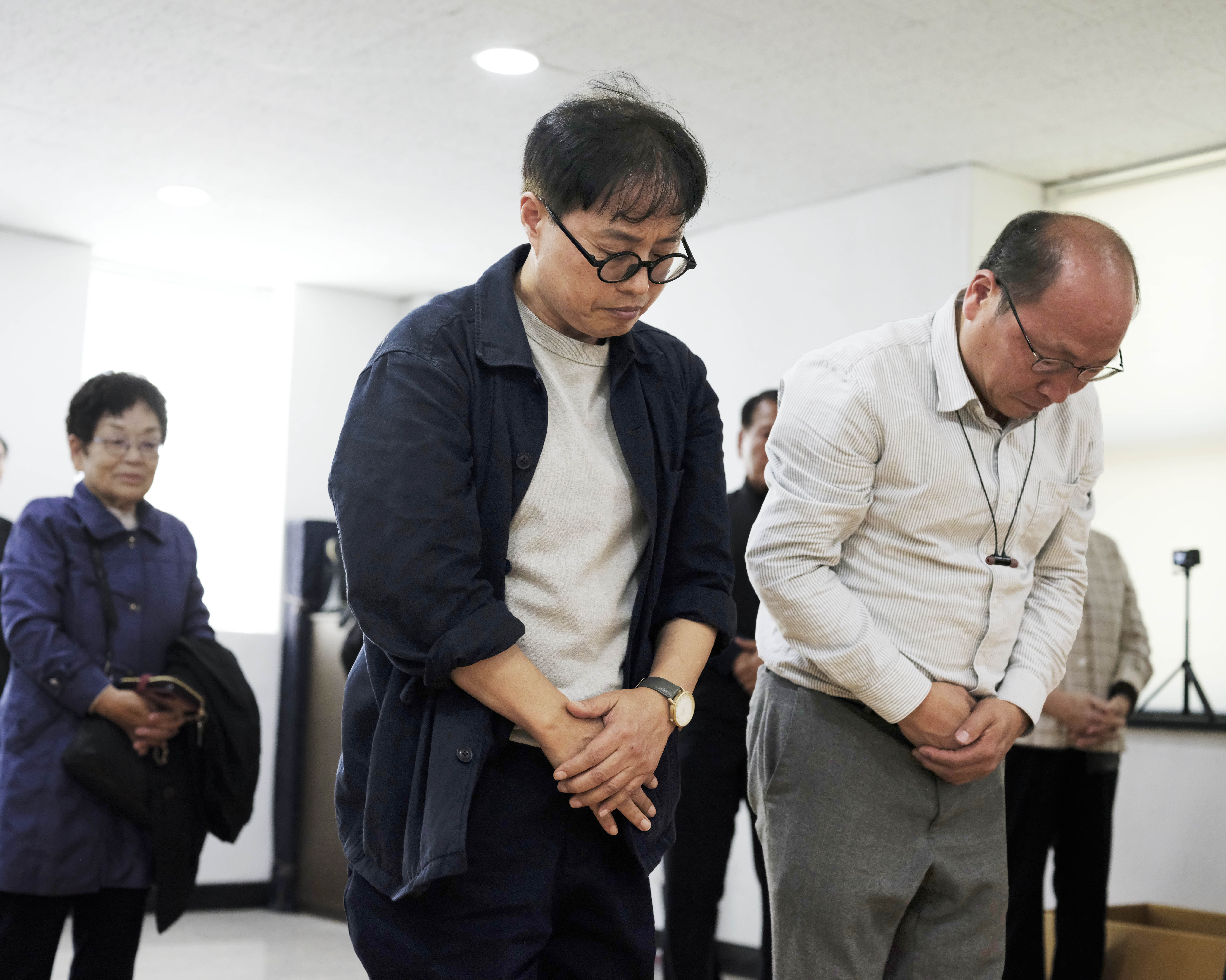 A photo of Sim Kyu Sang and Im Jae Geun bowing their heads down with their arms crossed in front of them.