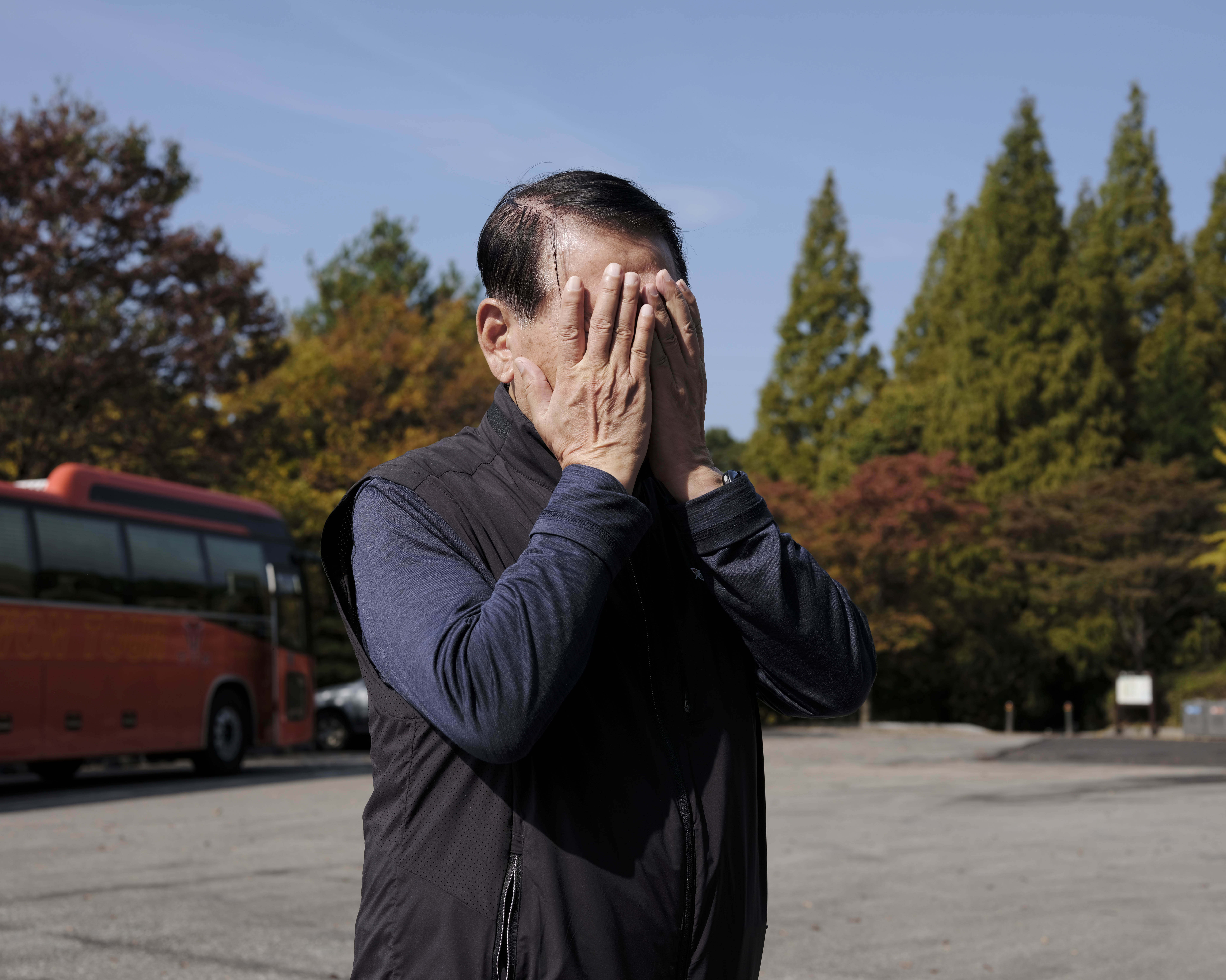 A man covers his face standing outside a bus.