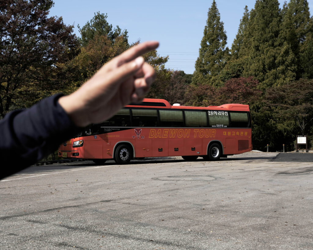 A photo of a Daewon tour bus with a hand pointing in the distance in the foreground.