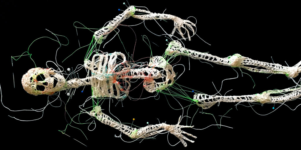 A photograph of an embroidered skeleton sculpture.