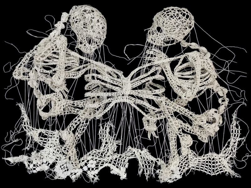 White embroidery on a black background of two skeletons connected by a shared ribcage.