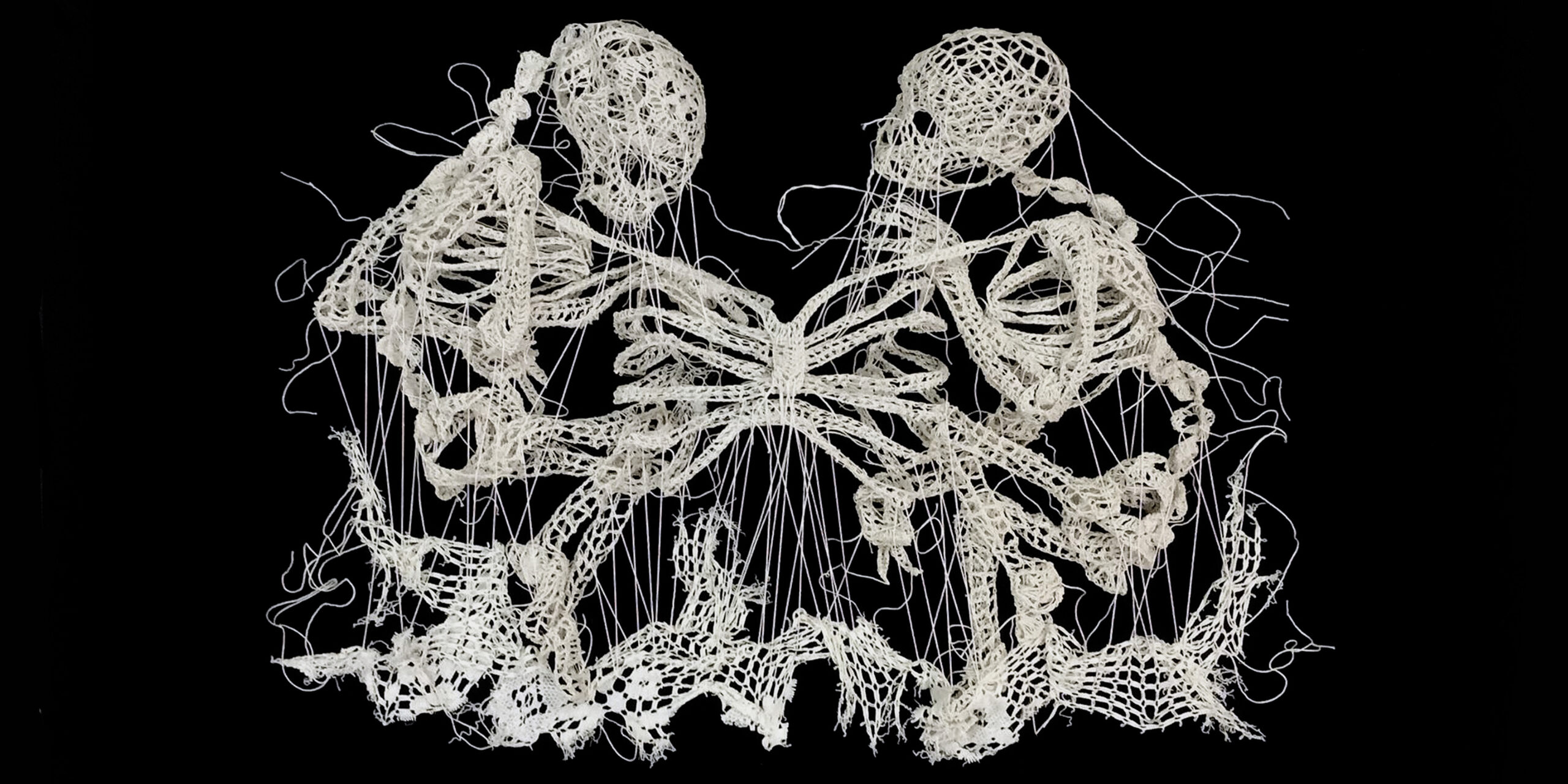 White embroidery on a black background of two skeletons connected by a shared ribcage.